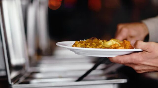 Kunde serviert sich selbst am Buffet eines indischen Restaurants einen gro&szlig;en Teller voll Essen