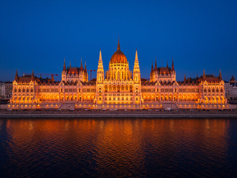 Aerial view of the illuminated Hungarian Parliament Building reflecting on the tranquil Danube River under a twilight sky, Budapest, Hungary. - Powered by Adobe