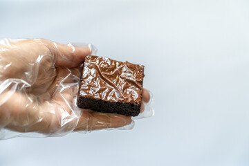 Gloved Hand Holding Single Brownie Against White Background