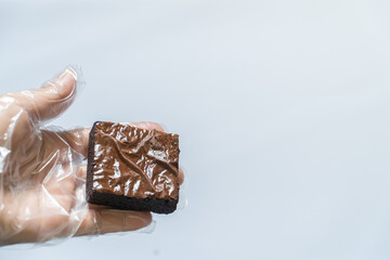 Gloved Hand Holding Brownie in Left Foreground on White Background