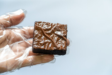 Gloved Hand Holding Unpackaged Brownie, Blurred Tray Background