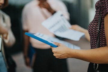 A diverse group of business professionals engaged in a discussion while reviewing documents outdoors in a city setting, showcasing teamwork and multicultural collaboration.