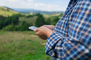 A close-up of a hiker's hands holding a smartphone, tracking a digital route marked by a dotted...