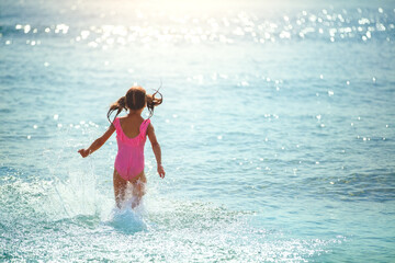 Active rest on the beach in summer. Happy little girl runs into the water. Child in pink swimsuit