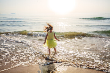 Happy little girl runs on the beach. The kid in the yellow dress