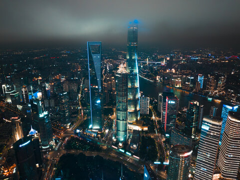 Shanghai, China - 21 June 2025: Aerial view of the city's illuminated skyscrapers piercing the misty night sky, the Huangpu River reflecting the vibrant urban glow.