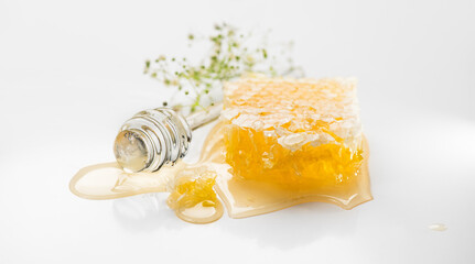 Fresh Honey in honeycombs dripping, pouring from a glass honey dipper spoon, on grey background. Honeycomb close-up. Healthy organic liquid honey spill, with flowers 