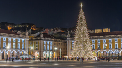 Obraz premium Commerce Square in Lisbon illuminated at Christmas hyperlapse, with a towering tree and crowds celebrating at night. Portugal