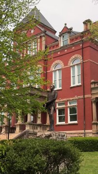 Vertical video of Fayetteville, West Virginia showcases its historic county courthouse with Romanesque architecture, complemented by a statue and lush greenery on a clear day.