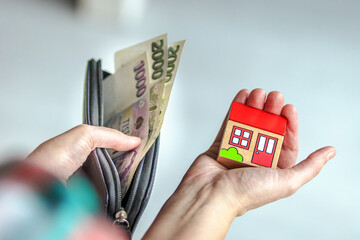 Hand holding a toy house and another hand holding Czech banknotes. Concept of real estate purchase,...