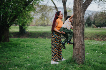 A caring mother supports her young child as they explore nature by climbing a tree in the park. The...