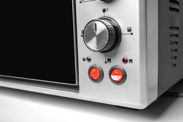 Close-up of red power switches and a control knob on a modern stainless steel electric oven,...