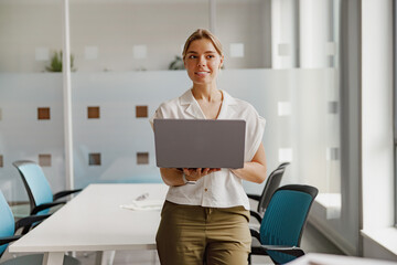 A confident and determined woman is holding a laptop, ready to engage in her work within a stylish...