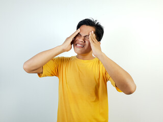 A young Asian man in yellow shirt is holding his head, showing signs of discomfort or a headache....
