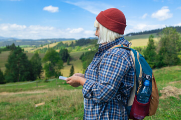 A close-up of a hiker's hands holding a smartphone, tracking a digital route marked by a dotted...