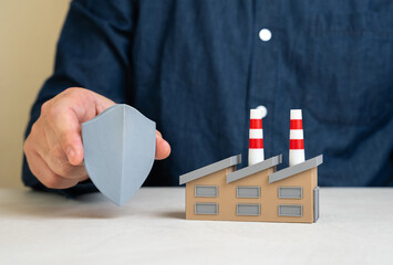 A man holds a protective shield near a factory. Risk management, insurance, and regulatory...
