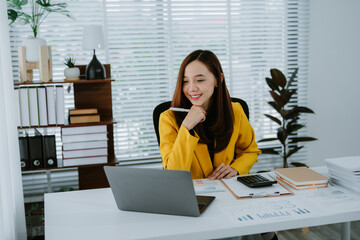 A beautiful Asian businesswoman analyzes charts using a laptop calculator at the office.