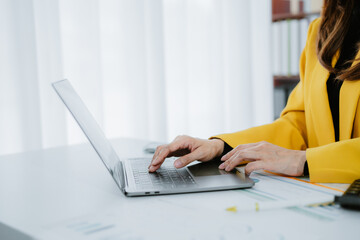 Portrait of a cheerful Asian businesswoman using a laptop and writing on a charger to keep notes as...