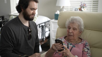 A grandson shows his grandmother how to use a smartphone to share photos, creating moments of happiness in their cozy home filled with memories.