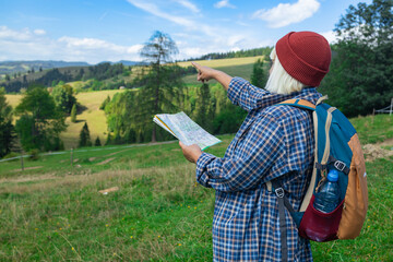 A young female traveler with a backpack stands on a grassy trail overlooking a beautiful rural...
