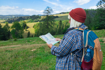 A young female traveler with a backpack stands on a grassy trail overlooking a beautiful rural...