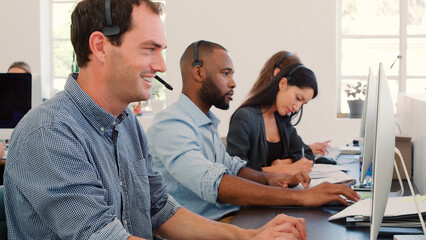 Multi-Cultural Business Team Wearing Headsets Working In Busy Customer Service Department