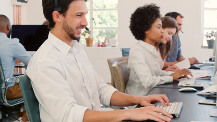 Multi-Cultural Business Team Wearing Headsets Working In Busy Customer Service Department