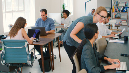 Multi-Cultural Business Team Working At Desks On Computers In Modern Open Plan Office