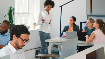 Obraz premium Multi-Cultural Business Team Working At Desks On Computers In Modern Open Plan Office
