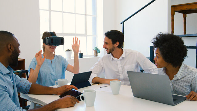 Multi-Cultural Business Team With Laptop And Virtual Reality Headset Having Meeting In Office