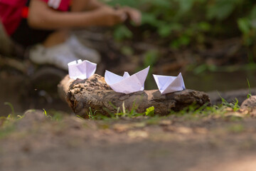 Three delicate paper boats are carefully resting on a rock that is located in the grassy area,...
