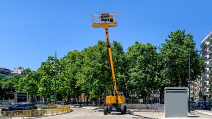 A towering yellow boom lift reaches skyward, evoking Arbor Day reverie and urban construction...