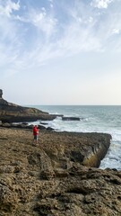 Solitary figure in crimson embraces untamed coastal wilderness, capturing oceanic whispers on World...