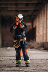 Wearing the helmet. Firefighter in professional equipment is indoors in abandoned building
