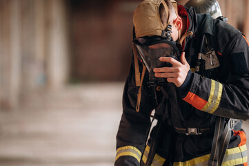 In mask, preparing air balloon. Firefighter in professional equipment is indoors in abandoned...