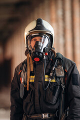 Protective air mask is on the face. Firefighter in professional equipment is indoors in abandoned...