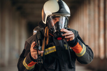 Protective air mask is on the face. Firefighter in professional equipment is indoors in abandoned...