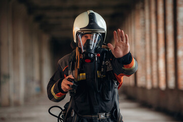 Stop hand gesture. Firefighter in professional equipment is indoors in abandoned building