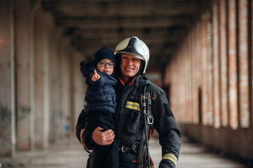 Modern hero is holding kid. Firefighter is with baby boy indoors