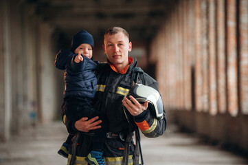 Modern hero is holding kid. Firefighter is with baby boy indoors