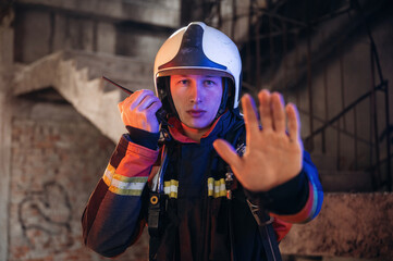 With walkie talkie radio. Firefighter in professional equipment is indoors in abandoned building