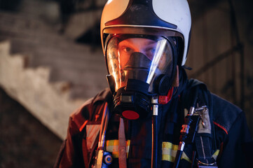 By the help of air mask. Firefighter in professional equipment is indoors in abandoned building