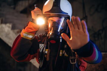 Flashlight, stop hand gesture. Firefighter in professional equipment is indoors in abandoned...