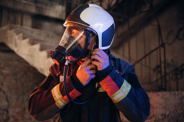 Ready, using a mask. Firefighter in professional equipment is indoors in abandoned building