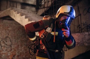 Adjusting air flow into the mask. Firefighter in professional equipment is indoors in abandoned...