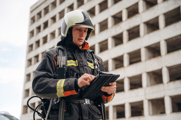 Black notepad is in hands. Professional firefighter is standing outdoors against big unfinished...