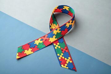 Autism awareness ribbon with colorful puzzle pieces on a split background of blue and grey