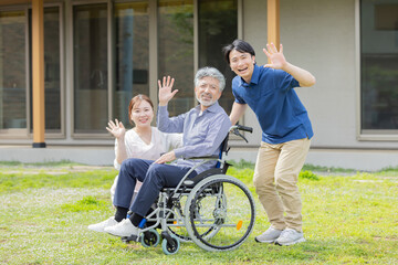住宅の前で手を振る車椅子に乗ったシニア男性とケアスタッフ