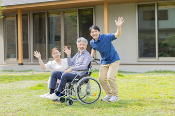 住宅の前で手を振る車椅子に乗ったシニア男性と介護士