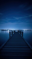 Fototapeta premium Wooden pier extending into calm water at dusk with city lights